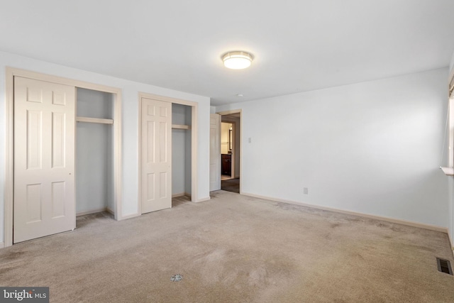 unfurnished bedroom with multiple closets and light carpet