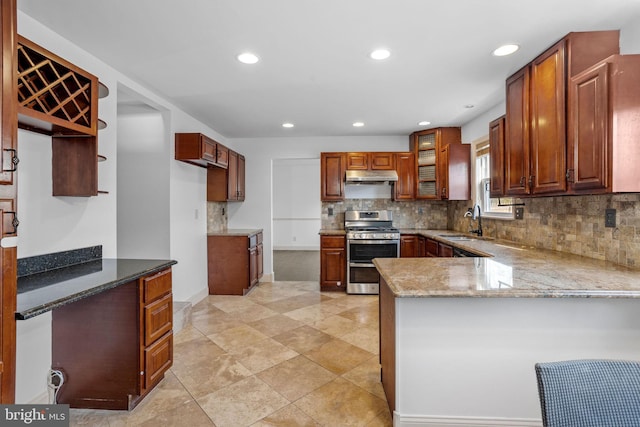 kitchen with kitchen peninsula, backsplash, stainless steel gas range oven, sink, and stone countertops