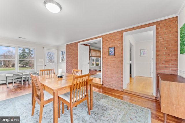 dining space with baseboard heating, crown molding, brick wall, and light hardwood / wood-style flooring