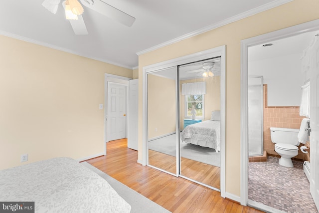 bedroom with ceiling fan, a baseboard radiator, hardwood / wood-style flooring, tile walls, and a closet