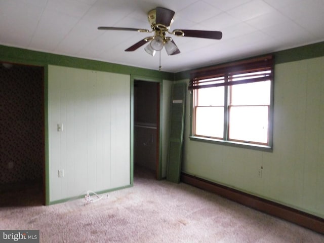 unfurnished bedroom featuring a spacious closet, light colored carpet, baseboard heating, and ceiling fan