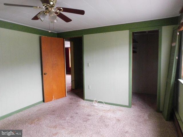 unfurnished bedroom featuring a walk in closet, a closet, light colored carpet, and ceiling fan