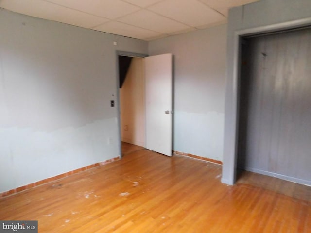 unfurnished bedroom featuring a paneled ceiling, hardwood / wood-style floors, and a closet