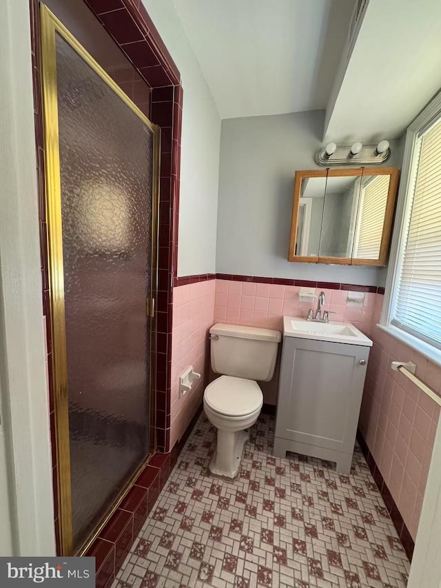 bathroom with toilet, tile walls, vanity, and a shower with shower door