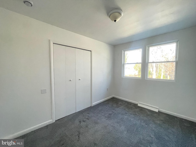 unfurnished bedroom with dark carpet, baseboard heating, and a closet