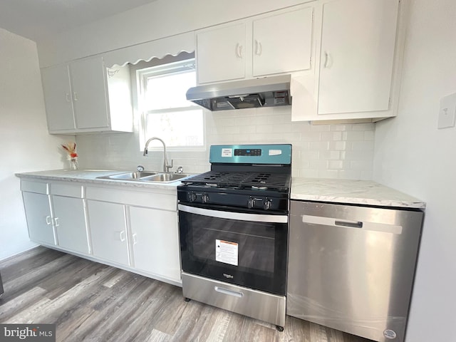 kitchen featuring stainless steel appliances, light countertops, a sink, light wood-type flooring, and under cabinet range hood