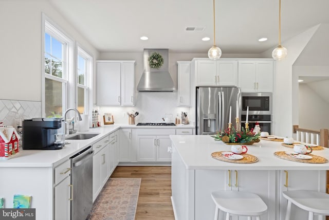 kitchen with a breakfast bar, stainless steel appliances, sink, wall chimney range hood, and decorative light fixtures