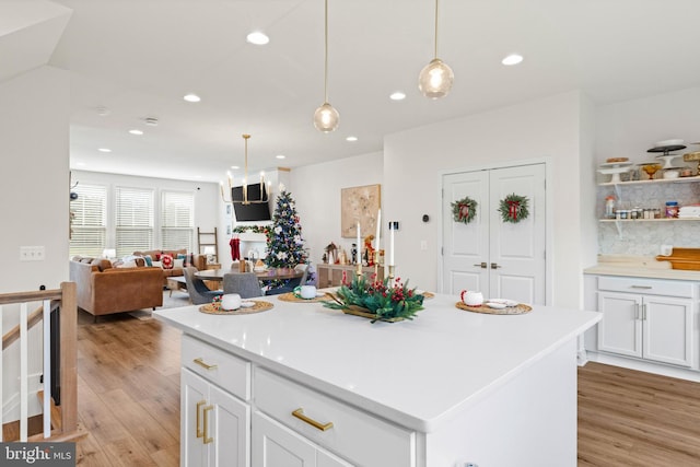 kitchen featuring a center island, backsplash, decorative light fixtures, white cabinets, and light wood-type flooring