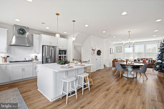 kitchen featuring wall chimney exhaust hood, white cabinetry, stainless steel appliances, and decorative light fixtures