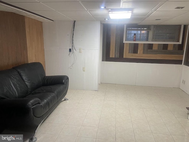 living area featuring a paneled ceiling, wooden walls, and light tile patterned flooring