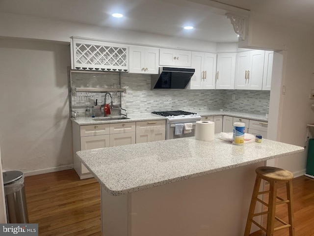 kitchen featuring hardwood / wood-style floors, exhaust hood, high end stainless steel range oven, sink, and white cabinetry