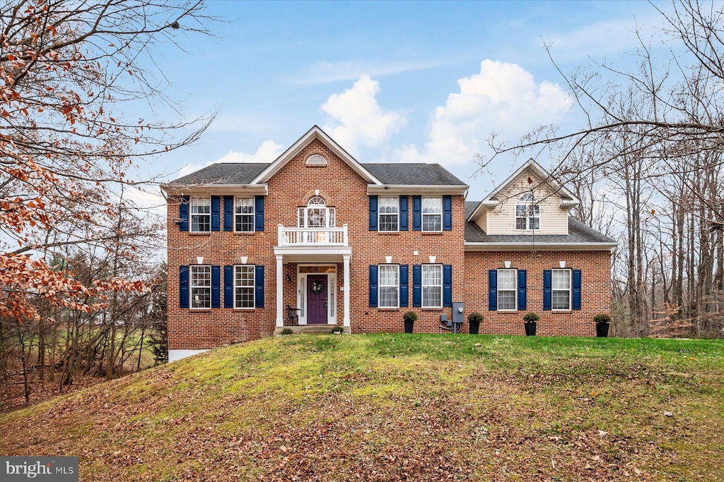 colonial home with a balcony and a front lawn