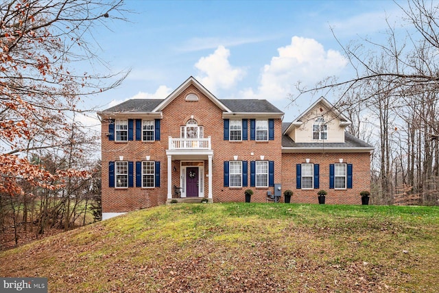 colonial home with a balcony and a front lawn