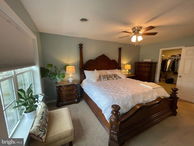 bedroom featuring a spacious closet, a closet, ceiling fan, and light carpet