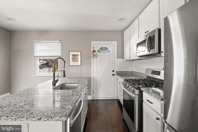 kitchen featuring light stone countertops, sink, stainless steel appliances, an island with sink, and white cabinets