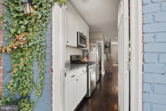 kitchen featuring white cabinets, appliances with stainless steel finishes, light stone countertops, and dark wood-type flooring