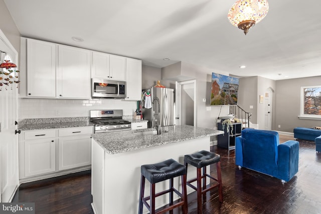 kitchen with white cabinets, a kitchen island with sink, dark wood-type flooring, and appliances with stainless steel finishes