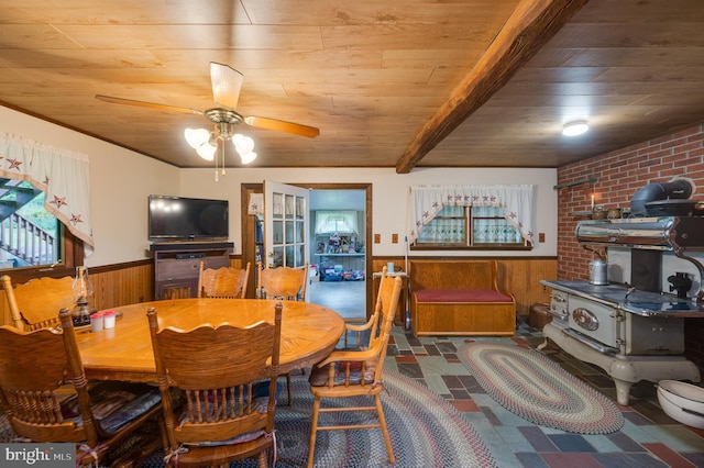 dining space with beamed ceiling, ceiling fan, wood ceiling, and wood walls