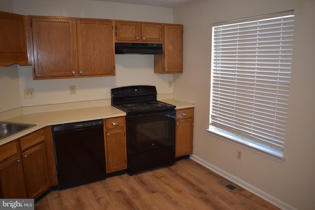 kitchen featuring black appliances, light wood-type flooring, sink, and range hood