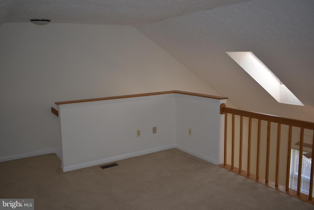 bonus room with light carpet, a textured ceiling, and vaulted ceiling with skylight