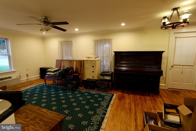 living room featuring ceiling fan with notable chandelier, wood-type flooring, ornamental molding, and a wall unit AC