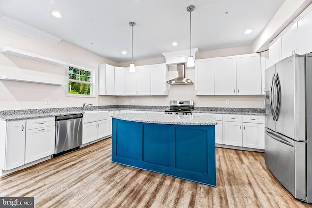 kitchen featuring stainless steel appliances, wall chimney range hood, decorative light fixtures, a center island, and white cabinetry