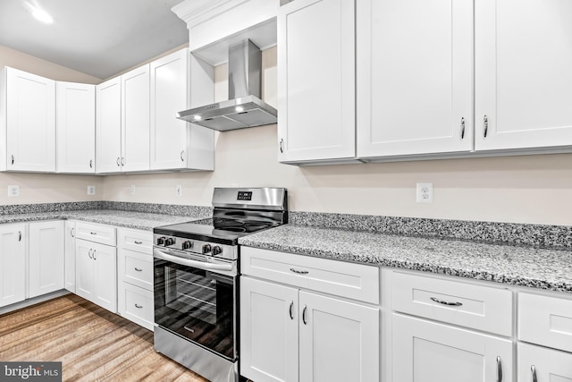 kitchen featuring wall chimney range hood, stainless steel stove, light stone countertops, light wood-type flooring, and white cabinetry