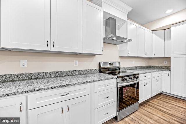 kitchen featuring wall chimney exhaust hood, white cabinets, and stainless steel stove