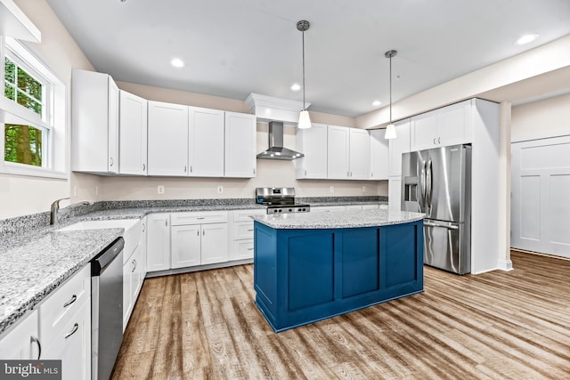 kitchen with wall chimney range hood, a kitchen island, light hardwood / wood-style floors, white cabinets, and appliances with stainless steel finishes