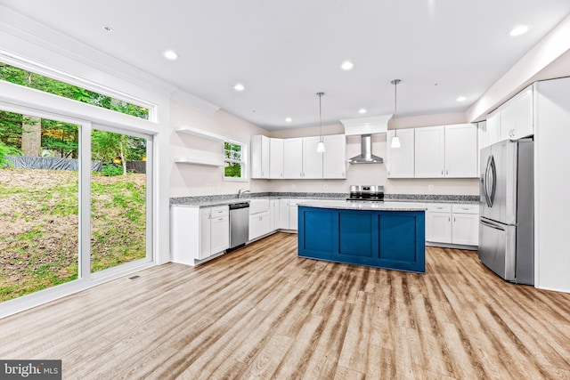 kitchen featuring white cabinetry, decorative light fixtures, wall chimney range hood, and appliances with stainless steel finishes