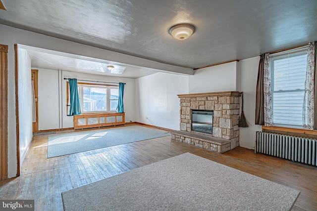 unfurnished living room featuring a stone fireplace, radiator heating unit, a textured ceiling, and light wood-type flooring