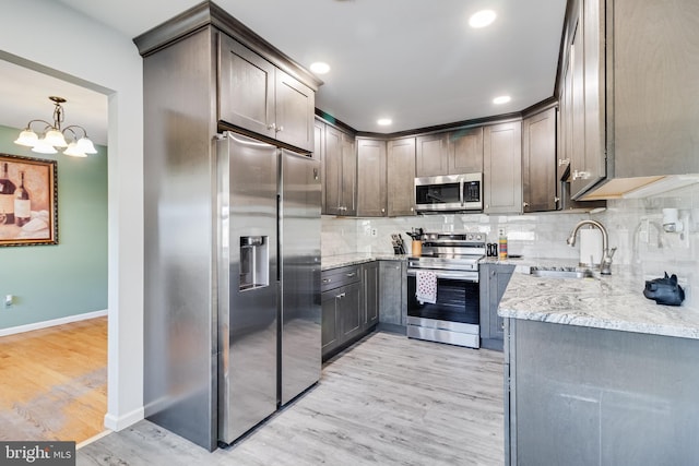 kitchen with appliances with stainless steel finishes, light stone counters, sink, light hardwood / wood-style flooring, and a notable chandelier