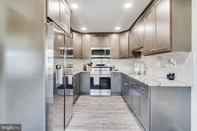 kitchen with light stone counters, stainless steel appliances, light hardwood / wood-style flooring, and sink