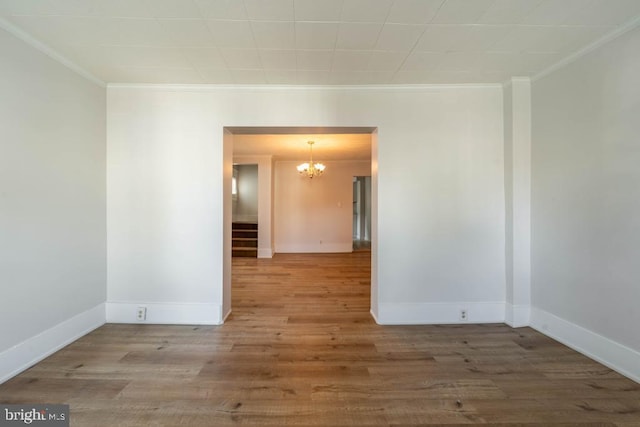 empty room with hardwood / wood-style flooring, crown molding, and an inviting chandelier