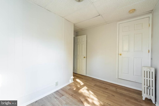 unfurnished room with radiator heating unit, a drop ceiling, and hardwood / wood-style flooring