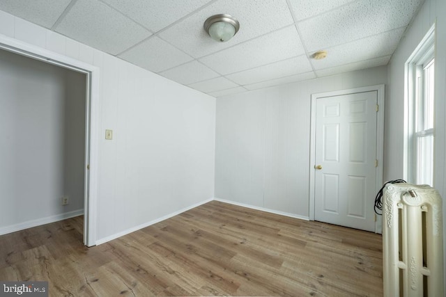 unfurnished room with radiator, a drop ceiling, and light wood-type flooring