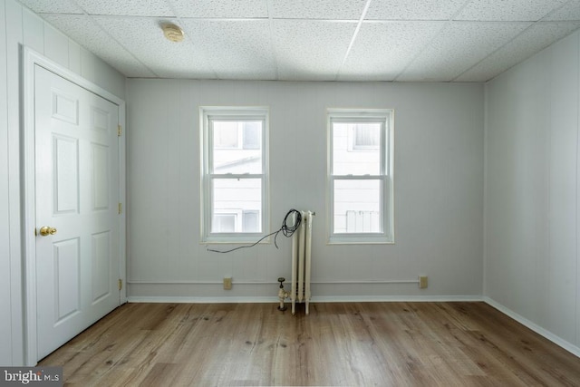 empty room with radiator heating unit, light hardwood / wood-style floors, and a drop ceiling