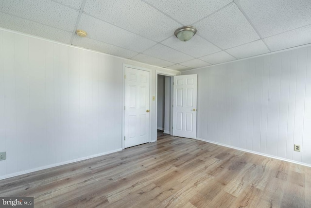 spare room with wood walls, a drop ceiling, and light hardwood / wood-style floors