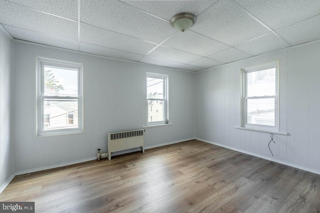 unfurnished room with a drop ceiling, light hardwood / wood-style floors, and radiator