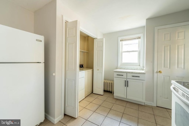 kitchen with white appliances, white cabinets, light tile patterned floors, radiator heating unit, and washing machine and clothes dryer