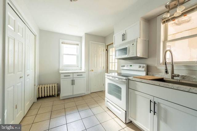 kitchen with white cabinetry, radiator heating unit, sink, white appliances, and light tile patterned flooring