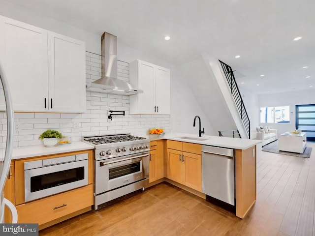 kitchen with light wood-type flooring, appliances with stainless steel finishes, sink, and wall chimney range hood