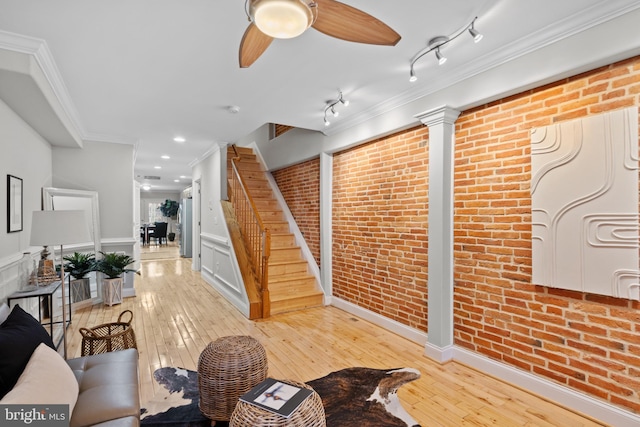 living room featuring light hardwood / wood-style flooring, rail lighting, brick wall, and ornamental molding