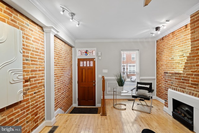 foyer entrance with light hardwood / wood-style flooring, brick wall, crown molding, track lighting, and a fireplace