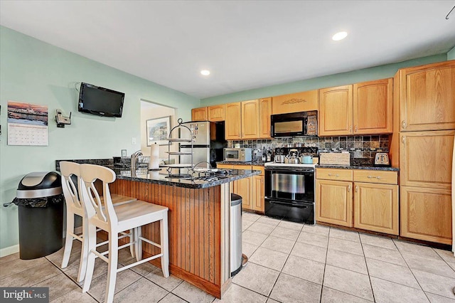 kitchen with backsplash, kitchen peninsula, a breakfast bar, light tile patterned floors, and black appliances