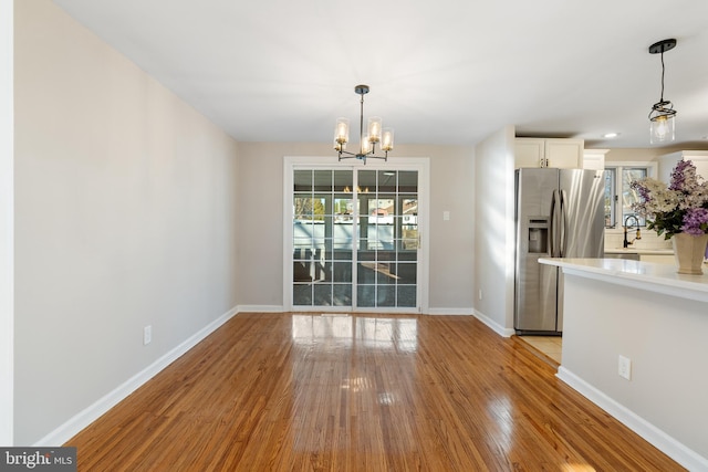 unfurnished dining area with light wood-type flooring, sink, and an inviting chandelier