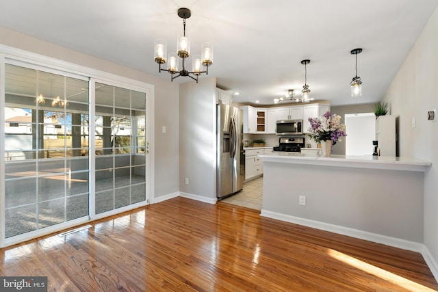 kitchen with an inviting chandelier, hanging light fixtures, light wood-type flooring, white cabinetry, and stainless steel appliances