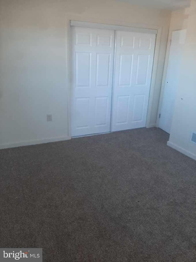 unfurnished bedroom featuring dark colored carpet and a closet