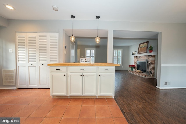 kitchen with white cabinetry, a brick fireplace, butcher block countertops, pendant lighting, and light tile patterned floors