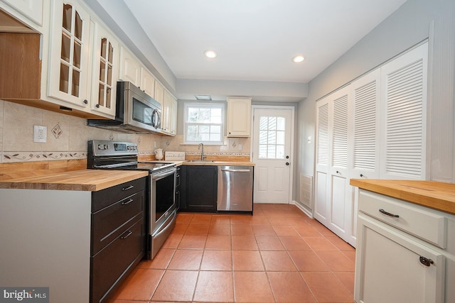 kitchen featuring wood counters, sink, light tile patterned floors, tasteful backsplash, and stainless steel appliances